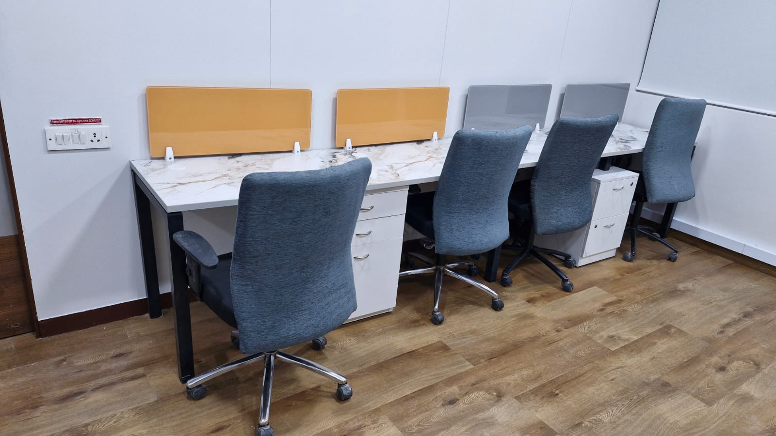 Close view of white workstations with grey task chairs, desk screens and lockable pedestals