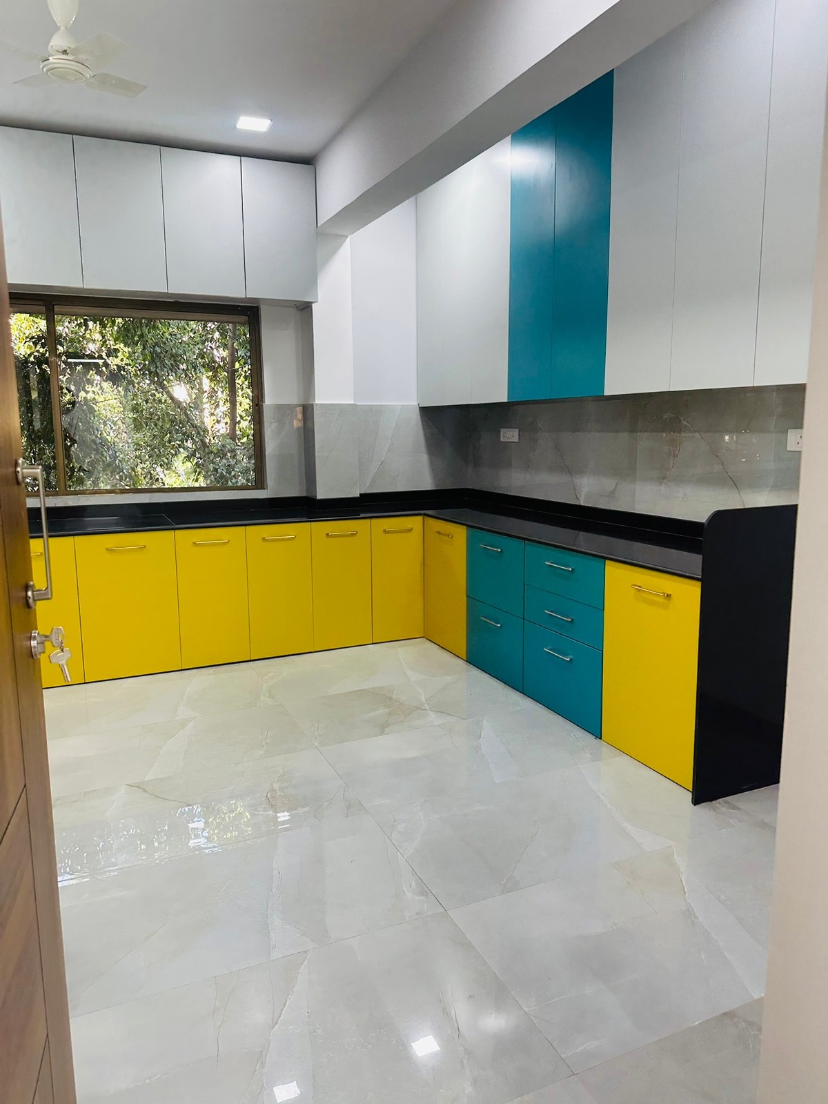 L-shaped modular kitchen with yellow and teal shutters, white wall units and a black counter