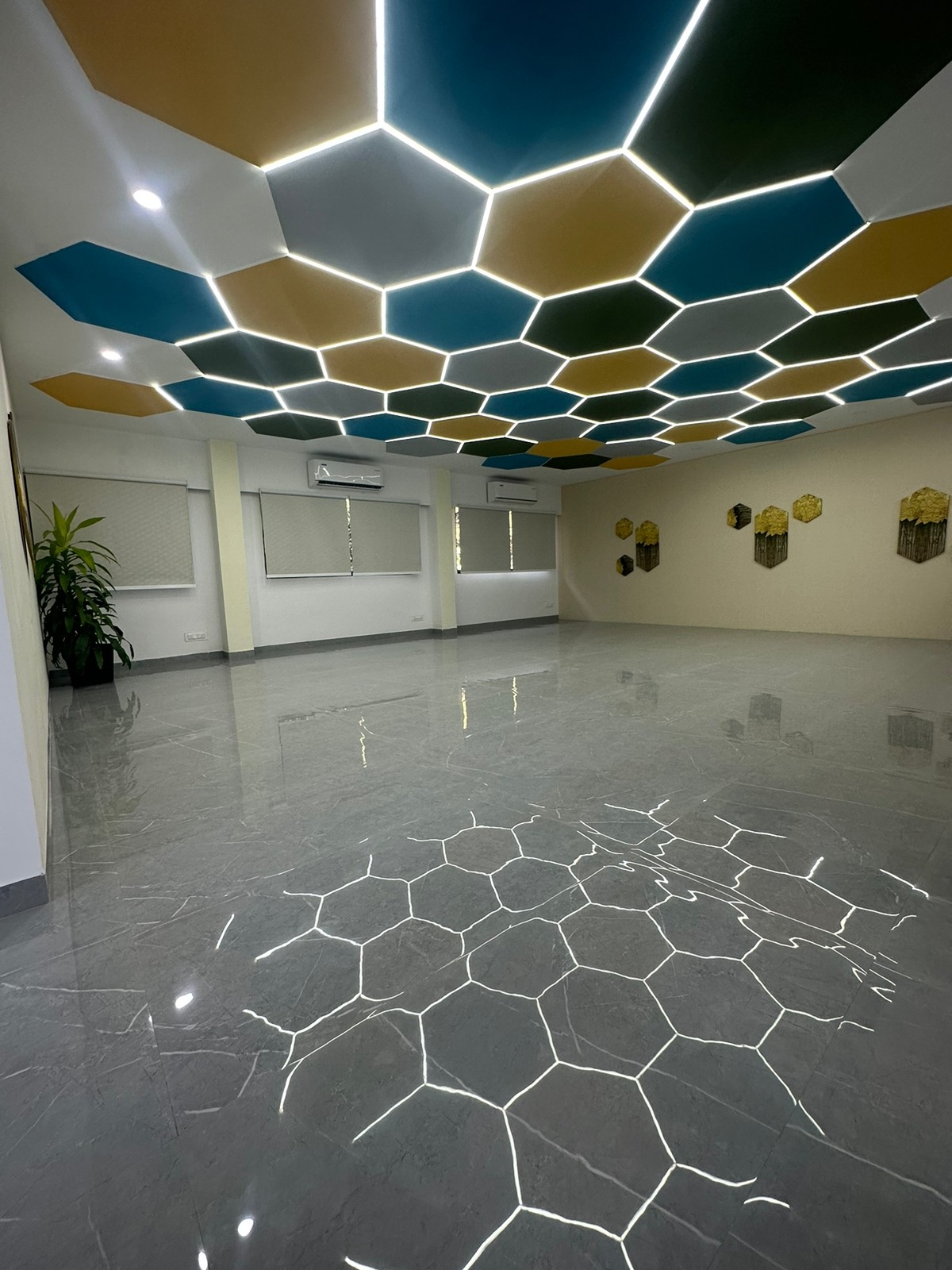 Room with a ceiling of teal, yellow and green hexagon panels and a hexagon pattern in the polished floor